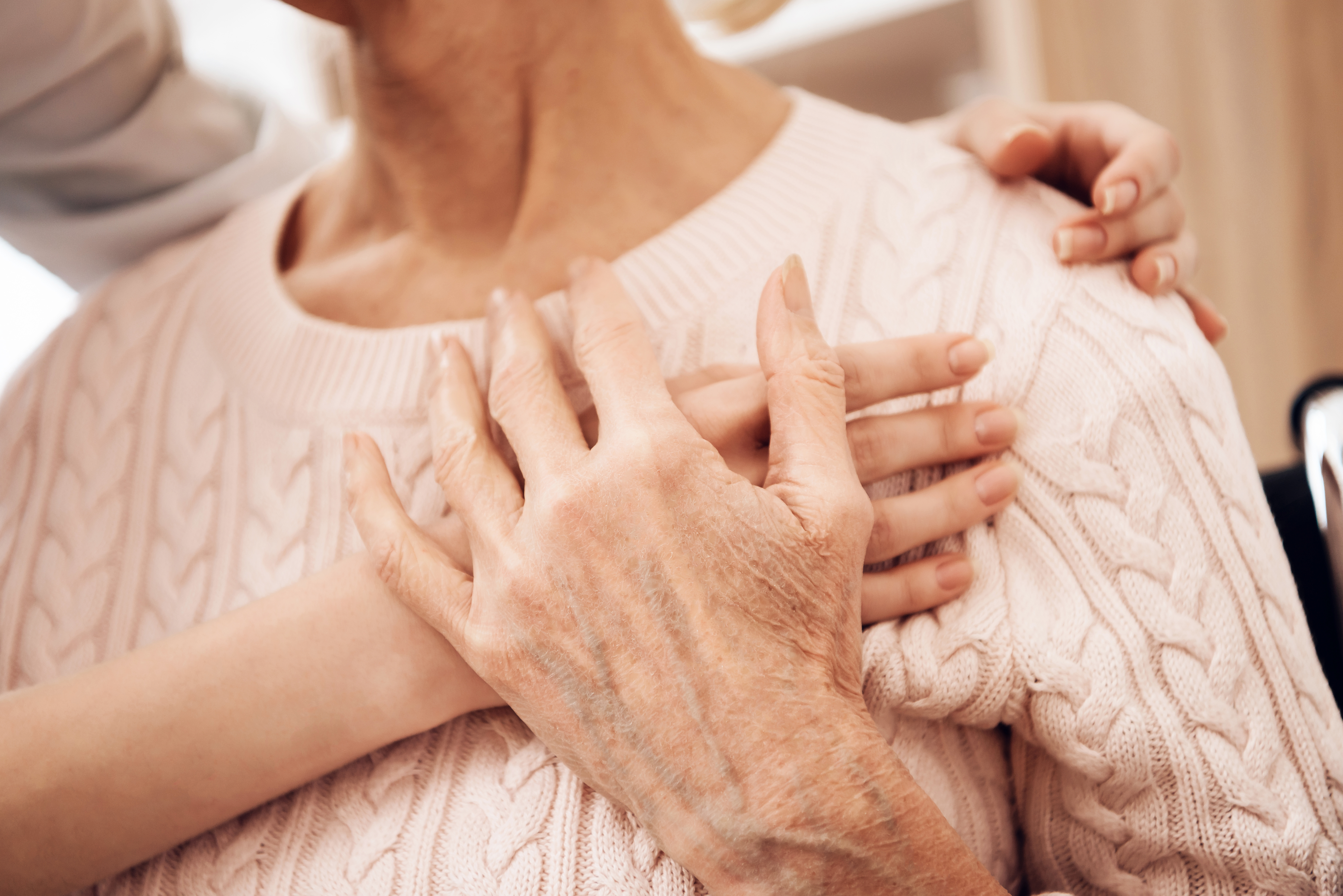 24-Stunden-Betreuung. Eine junge Frau umarmt eine ältere Dame, die dankend die Hand der jungen Frau berührt.