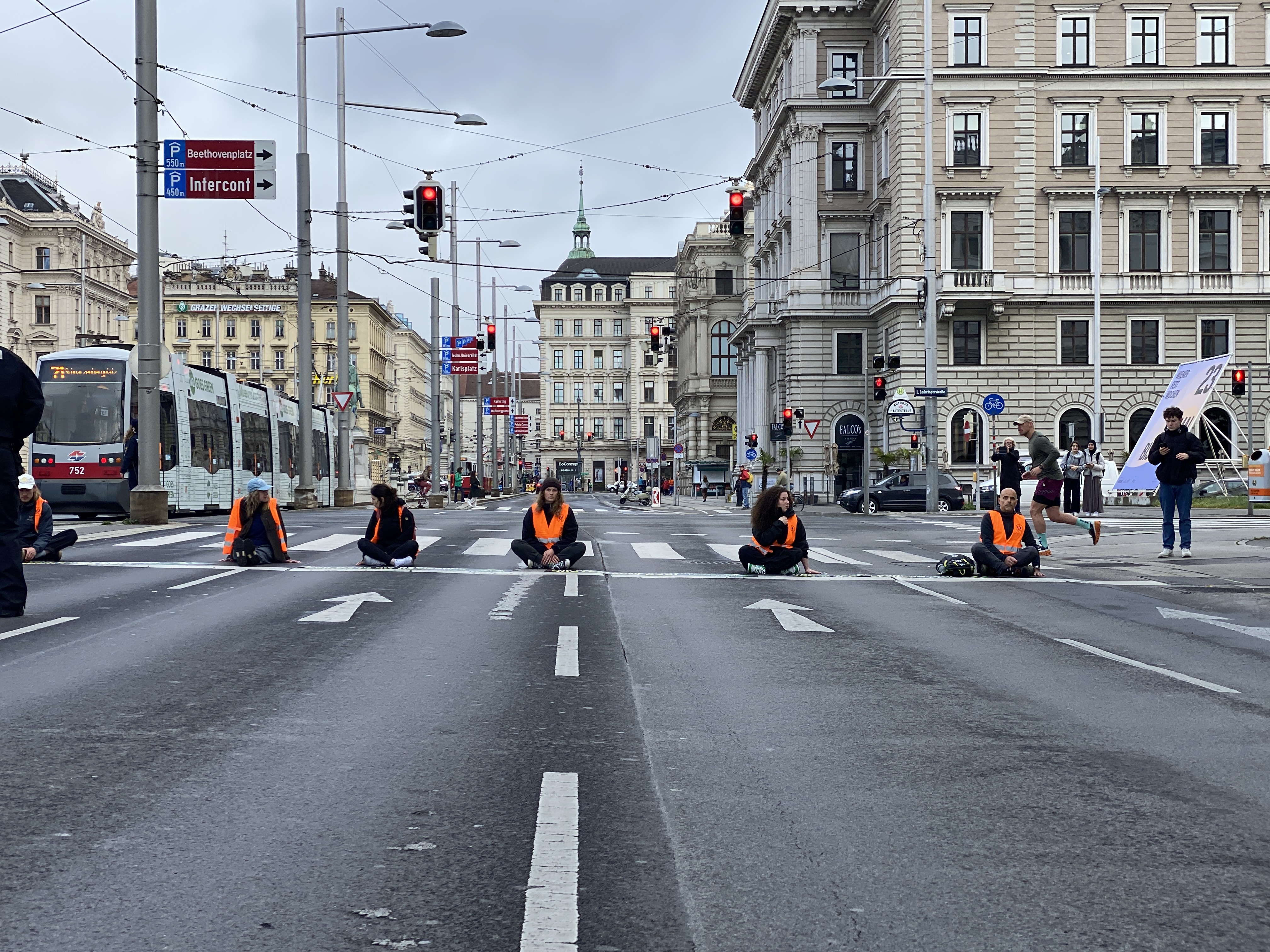 Klimaschutz zu fordern, ist kein Verbrechen. Man sieht Klimaaktivist:innen der Letzten Generation, die auf einer Straße am Boden sitzen. Sie tragen orange Warnwesten.