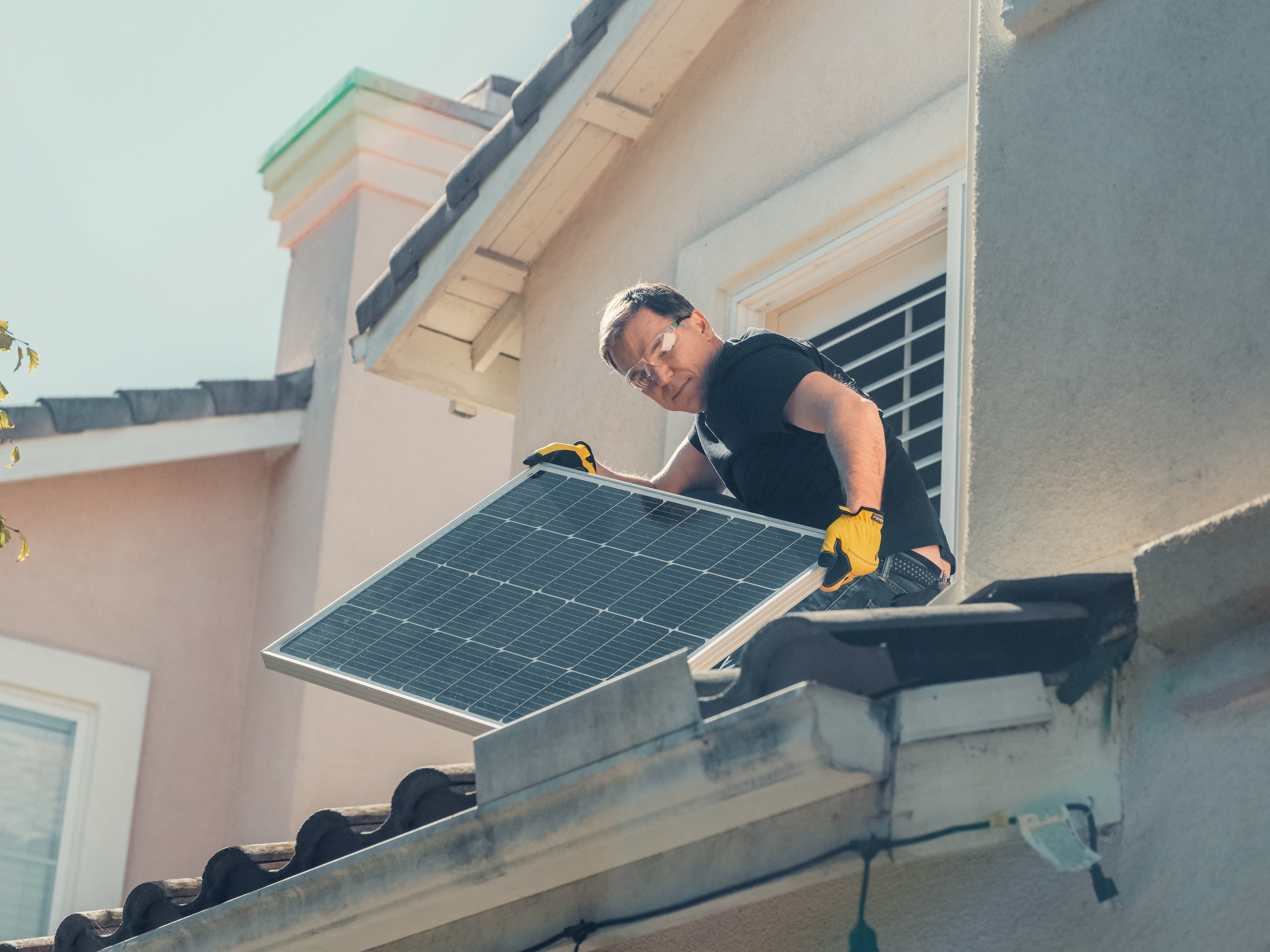 Ein Mann montiert auf einem Dach eine Photovoltaik-Anlage.