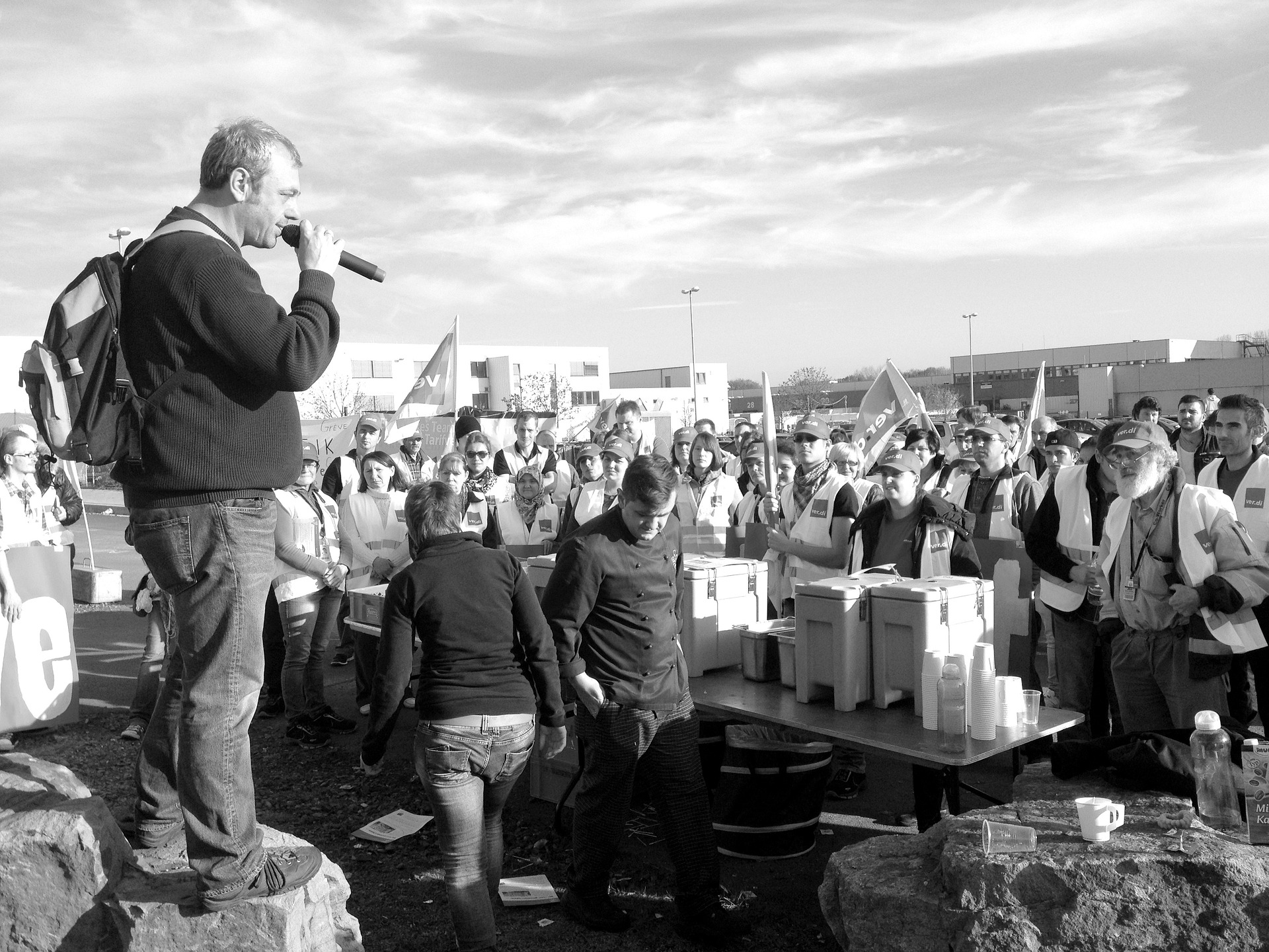 Man sieht ein schwarz-weiß Bild von einem Mann mit Mikrofon, der zu einem Protest-Publikum spricht.
