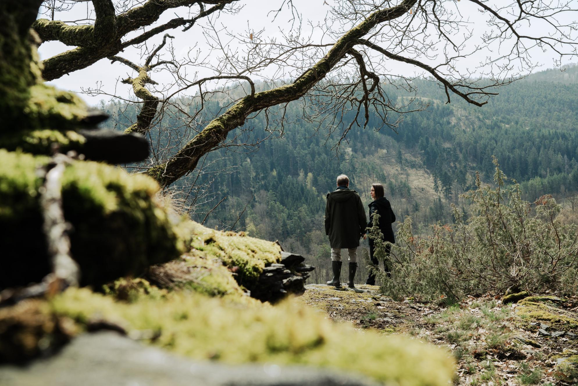 Zu sehen sind zwei Personen, die Autorin des Artikels, Lisa Wohlgenannt, im Gespräch mit einem Forst Experten. Die beiden stehen an einem Aussichtspunkt, umrahmt von Natur und in die Weite der Hügellandschaft der Wälder