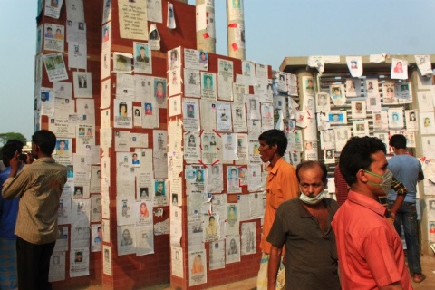Eine Wand mit Fotos von Vermissten nach dem Gebäudeeinsturz der Textilfabrik Rana Plaza in Sabhar. Ein <span class=