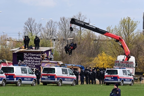 Bild zeigt Kran, der Menschen von Gebäude trägt, davor Polizei und Fahrzeuge.