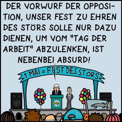 Man sieht das Podium von weiterer Entfernung. Über Plenk hängt ein Banner auf dem steht “1. Mai = Fest des Störs”. Vor ihm stehen viele Menschen. Plenk sagt: “Der Vorwurf der Opposition, unser Fest zu Ehren des Störs solle nur dazu dienen, um vom “Tag der Arbeit” abzulenken, ist nebenbei absurd.”