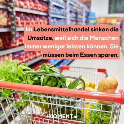 In einem Einkaufswagen liegen Produkte, wie etwa ein Salat und Kartoffeln. Er fährt in einem Gang im Supermarkt, in den Regalen sieht man Nudelpackungen. Im Lebensmittelhandel sinken die Umsätze, weil sich die Menschen immer weniger leisten können. Sie müssen beim Essen sparen.