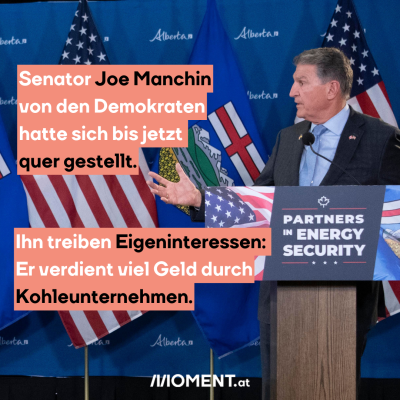 Ein Mann steht hinter einem Podest, auf dem “Parnters in Energy Security” steht. Hinter ihm sind die Flaggen der USA und des kanadischen Bundesstaates Alberta zu sehen. Er blick nach links und hat die Hand erhoben. Es handelt sich um Joe Manchin. “Senator Joe Manchin von den Demokraten hatte sich bis jetzt quer gestellt. Ihn treiben Eigeninteressen: Er verdient viel Geld durch Kohleunternehmen.”