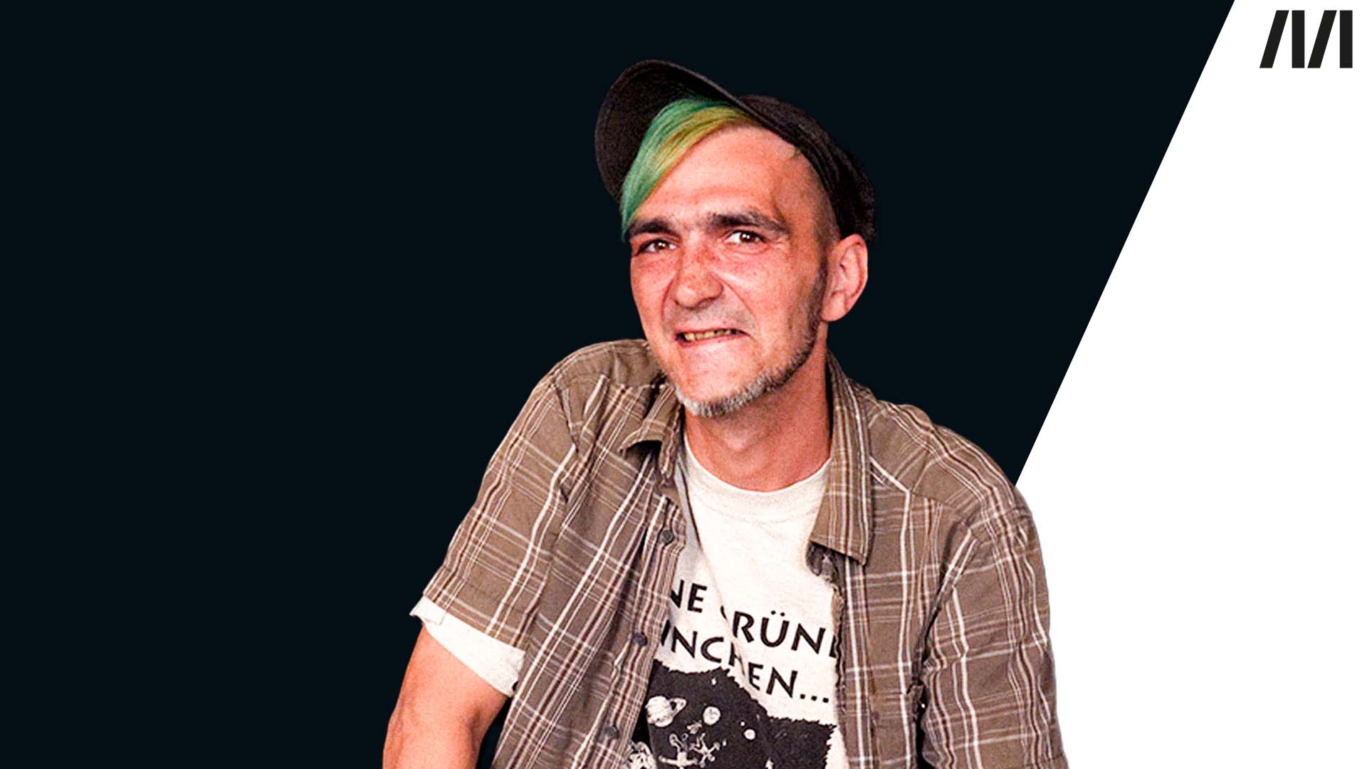 Foto eines lächelnden Mannes mit Hut und grün gefärbten Haaren