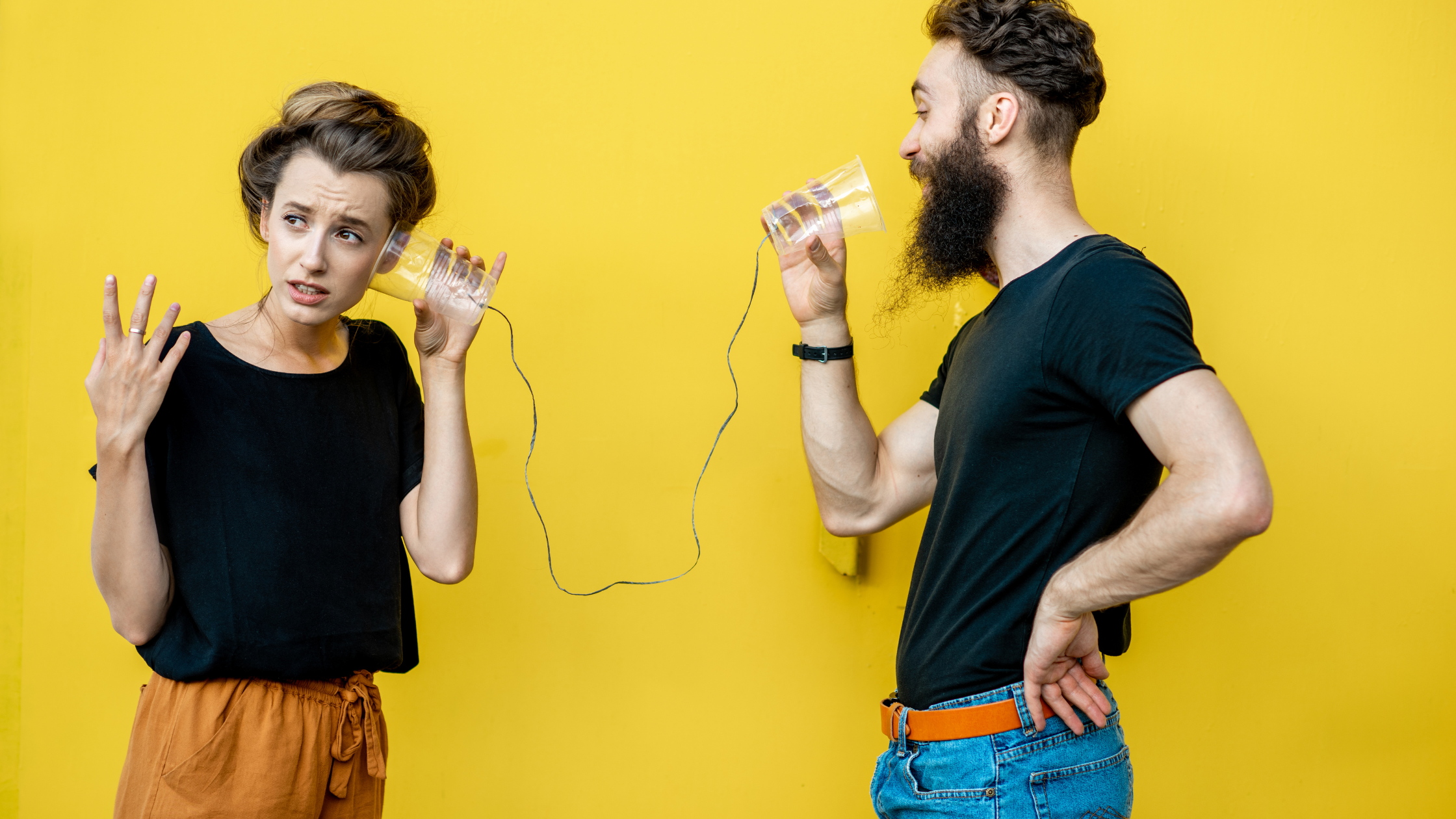 Argumente zum Gendern: Ein Mann und eine Frau stehen vor gelbem Hintergrund. Er spricht in ein Dosentelefon, sie hört mit aufgeregtem Gesichtsausdruck am anderen Ende.