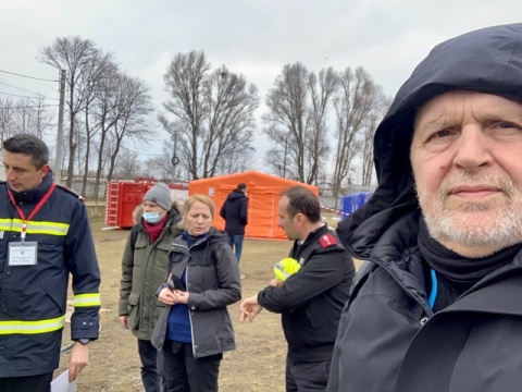 Zu sehen ist Herbert Paulischin, der ernst in die Kamera blickt. Im Hintergrund sind Menschem, ein Zelt und Bäume.