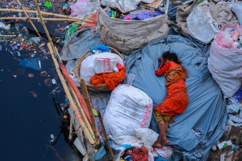 Eine Frau schläft an einem verschmutzten Flußbeet in Dhaka, Bangladesh