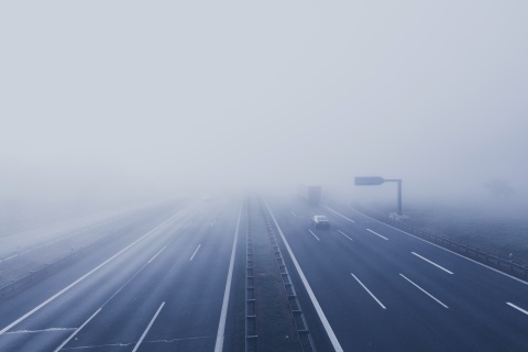 Luftaufnahme einer nebelvergangenen Autobahn mit wenigen Fahrzeugen und einer Ausfahrt.