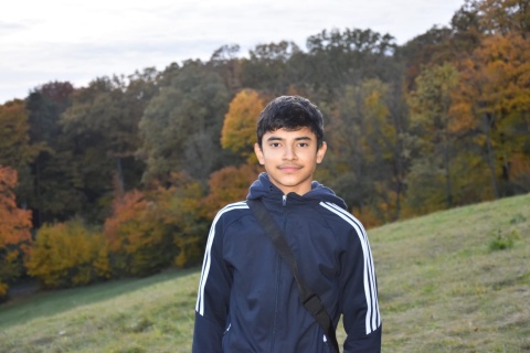 Emran steht im Trainingsanzug mit einer Tasche um die Schulter auf einer Wiese. Emran ist 14, Arbeiterkind und möchte studieren, um Bauingenieur zu werden.