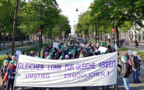 Eine Gruppe Menschen blockiert den Ring, auf einem Transparent das sie in die Höhe halten ist "Gleicher Lohn für Gleiche Arbeit. Umstieg ermöglichen!" zu lesen.