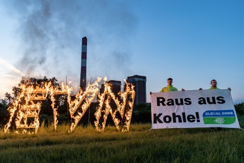 Foto von einer Aktion von Global 2000 Kohleausstieg zeigt zwei Aktivisten mit einem Transparent auf dem Raus aus Kohl steht vor einem Kohlekraftwerk stehend. Neben den Aktivisten steht ein übergroßes EVN Logo in Flammen.