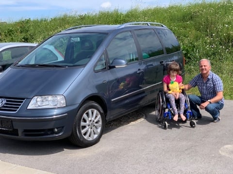 Mechaniker Hans Eidenhammer und Lily, im Rollstuhl sitzend, posieren vor dem neuen Auto.