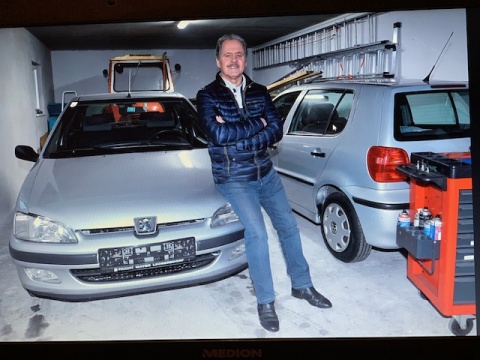 Der Mechaniker Hans Eidenhammer vor zwei Autos, die er repariert und verschenkt.