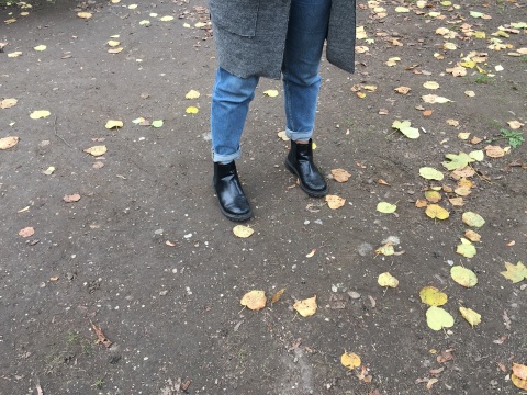 Auf dem Foto zu sehen sind Salmas Schuhe, schwarze Boots. Sie steht in einem Park.