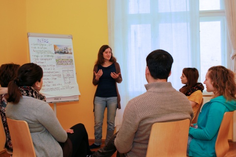 Sarah Zeller von Juno, Gemeinschaftliches Wohnen für Alleinerziehende, bei einem Infoworkshop. Sie spricht neben einem Flipchart stehend zu einer im Sesselkreis sitzenden Gruppe.