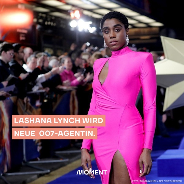 Lashana Lynch in einem rosa Kleid mit ernstem Blick.