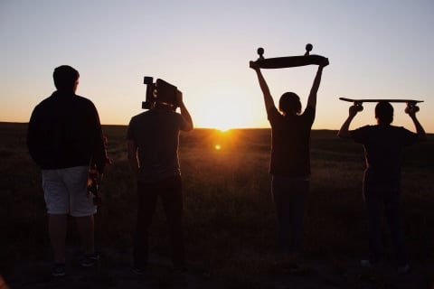 Vier junge Menschen die Skateboards über ihren Köpfen tragen blicken in den Sonnenuntergang.