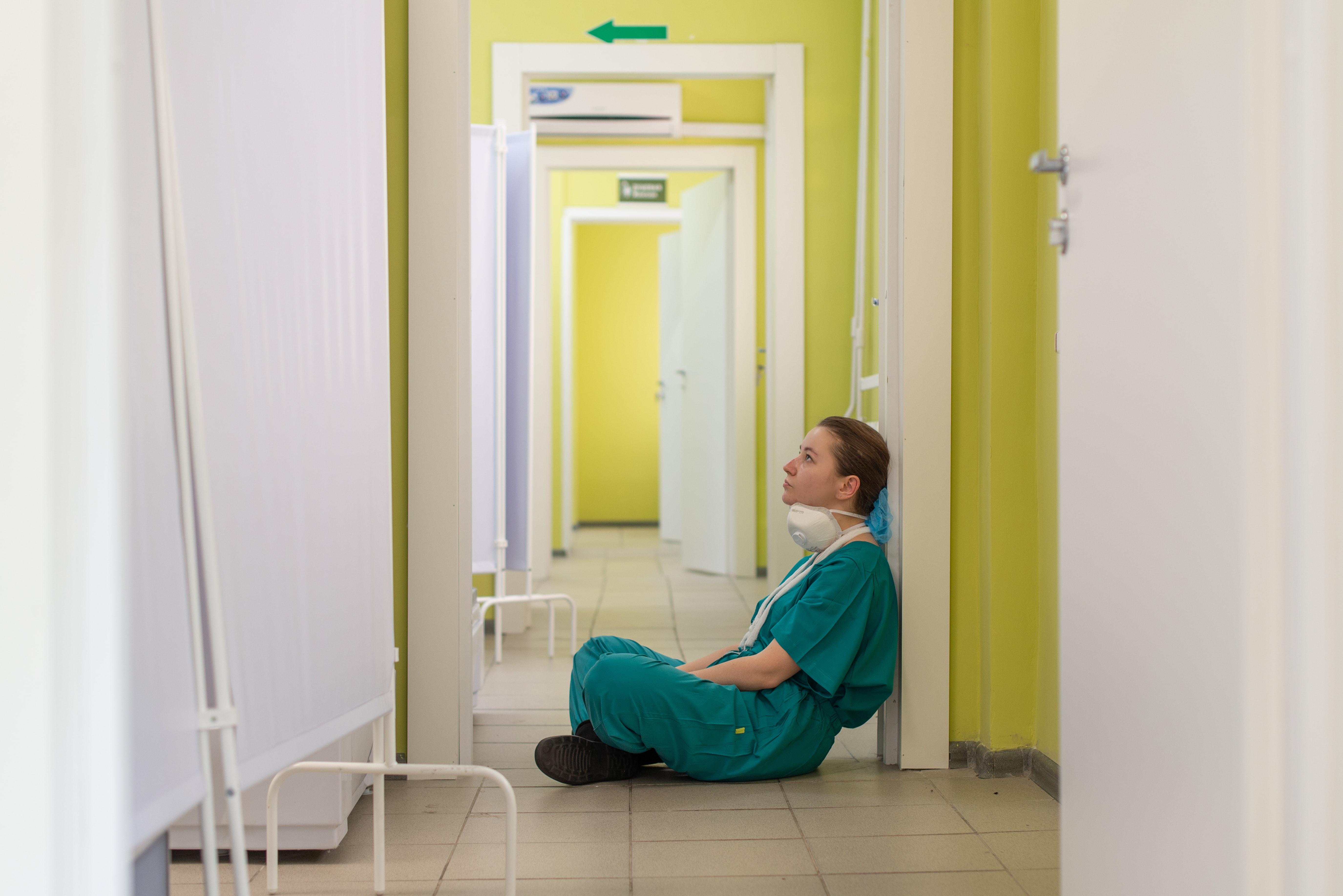 Eine Krankenschwester sitzt erschöpft und mit Tränen in den Augen am Boden eines Spitals.