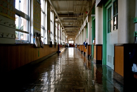Symbolbild zu Schulschließungen: Ein leerer Gang eines Schulgebäudes. Die Taschen, die an den Wänden hängen verraten: Die SchülerInnen sind wohl in den Klassen.