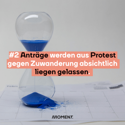 Eine Sanduhr mit blauem Sand, der zur Hälfte bereits durchgerunnen ist. Im Text: "#2 Anträge werden aus Protest gegen Zuwanderung absichtlich liegen gelassen."