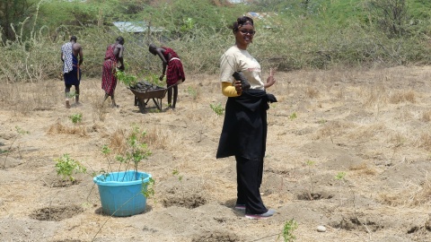 Mana Omar hilft, Bäume zu pflanzen. Im Hintergrund sind zwei Frauen zu sehen.