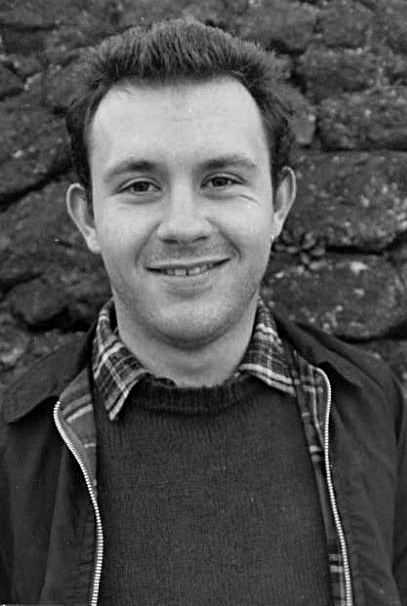 Man sieht ein schwarz-weiß Portrait von Mark Ashton. Er trägt eine Bomberjacke und blickt direkt in die Kamera.