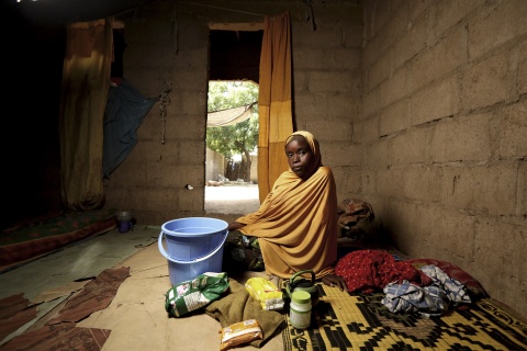 Bild zeigt eine geflohene Nigeria, die in einer einfachen Hütte auf dem Boden sitzt, ihre wenigen Habseligkeiten vor sich ausgebreitet.