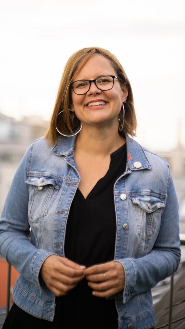 Andrea Brunner lacht und sieht direkt in die Kamera. Sie trägt eine Brille und eine Jeans-Jacke.