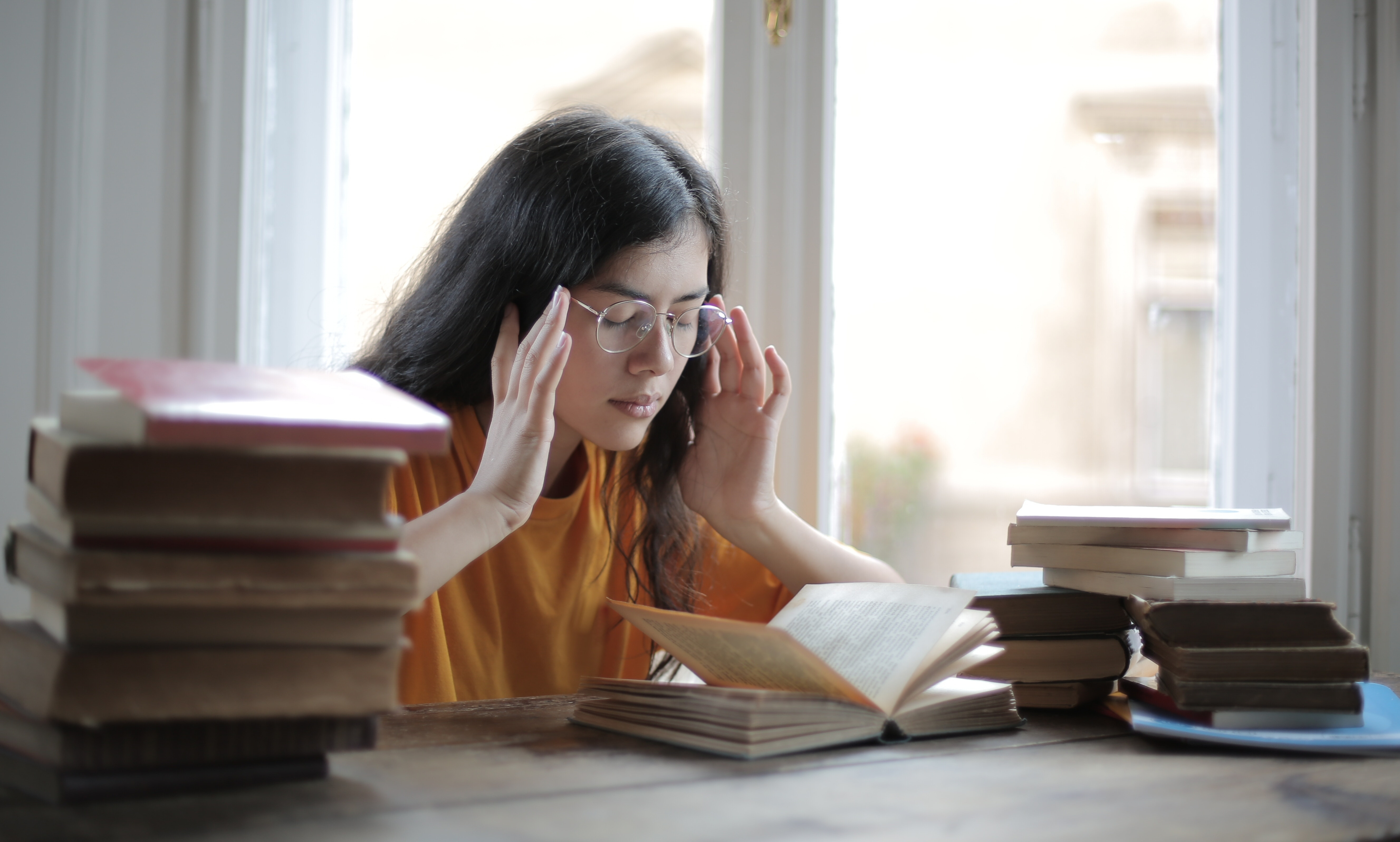 Eine Frau sitzt zwischen Bücherstapeln und sieht verzweifelt aus