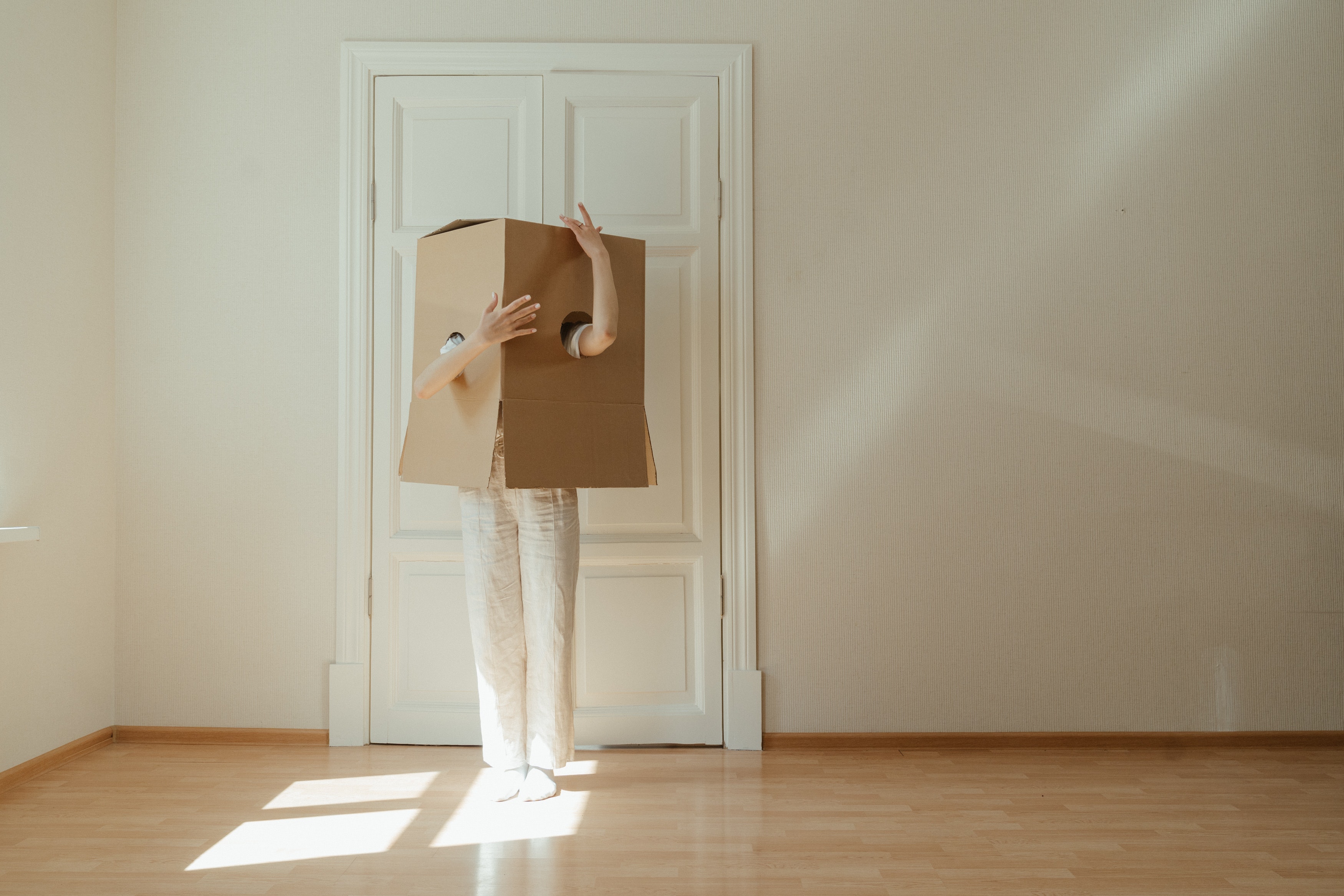 Eine Person steht in einer leeren Wohnung mit einem Karton über ihrem Kopf.