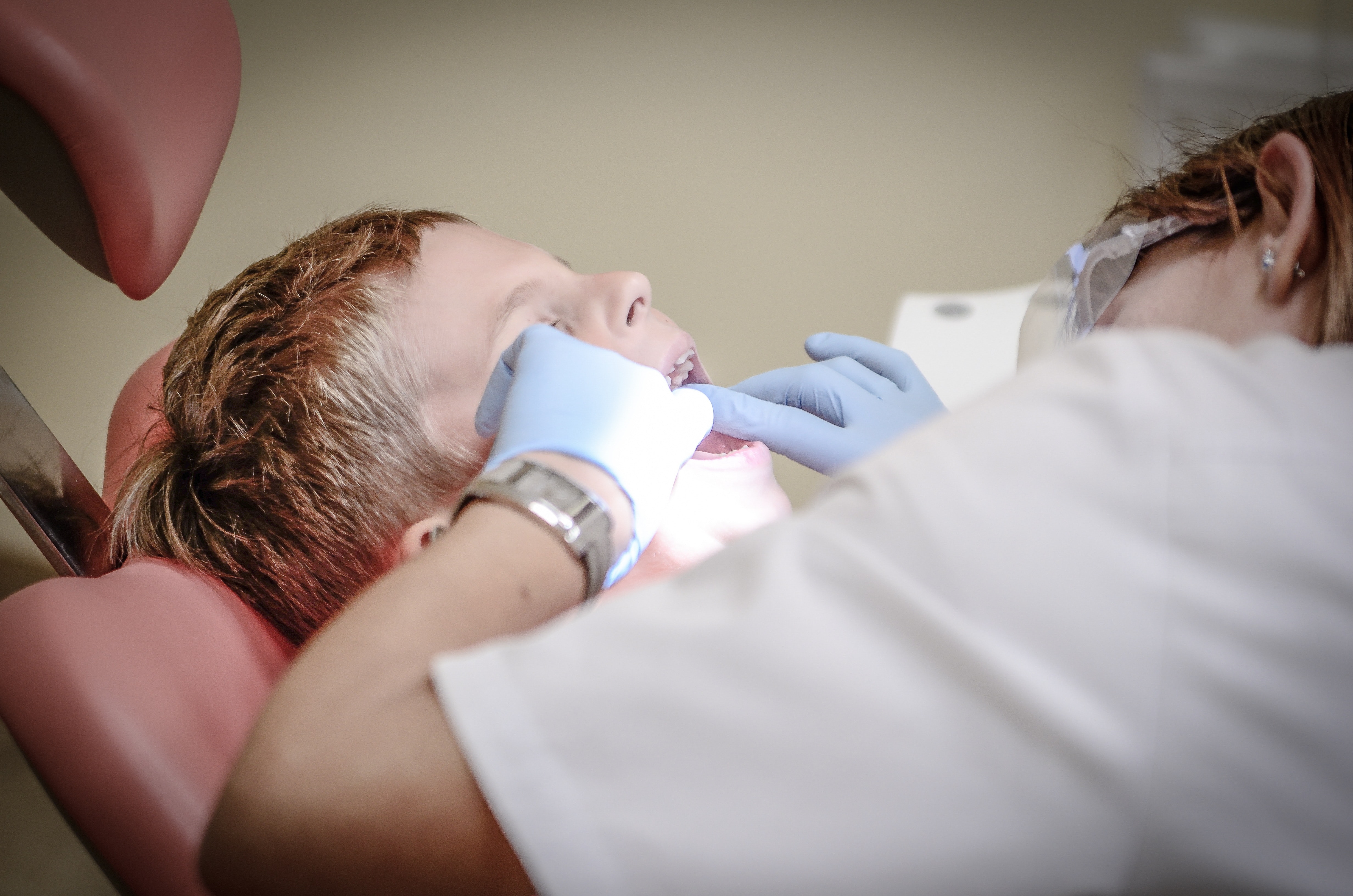 Ein Kind beim Zahnarzt, welcher im Mund des kleinen Patienten eine Kontrolle durchführt.