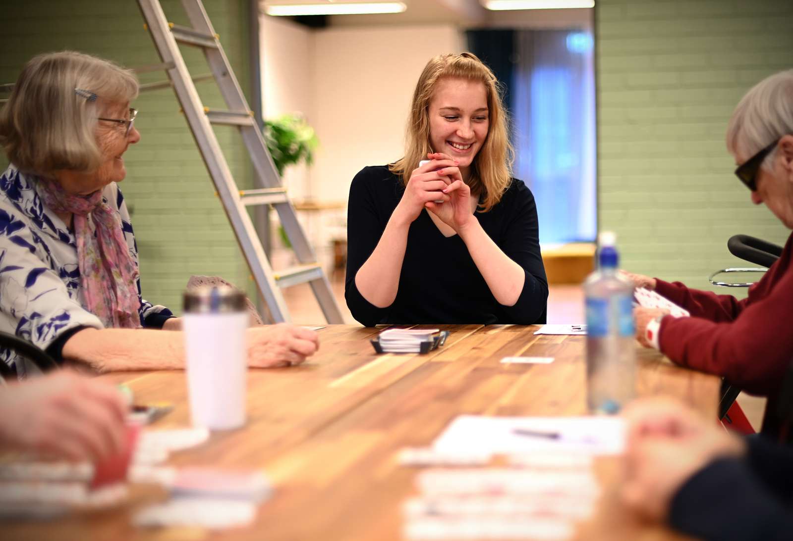 Alt und Jung gemeinsam im Wohnprojekt "SallBö". Eine junge Frau sitz mit drei alten Damen an einem Tisch. Sie spielen Karten und lachen herzlich.