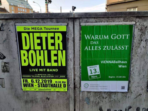 Foto von zwei Veranstaltungsplakaten, die auf einem Stromkasten kleben. Links die Ankündigung eines Dieter Bohlen Konzerts, rechts eine Veranstaltung der Stiftung Gralsbotschaft unter dem Titel "Warum Gott das alles zulässt."