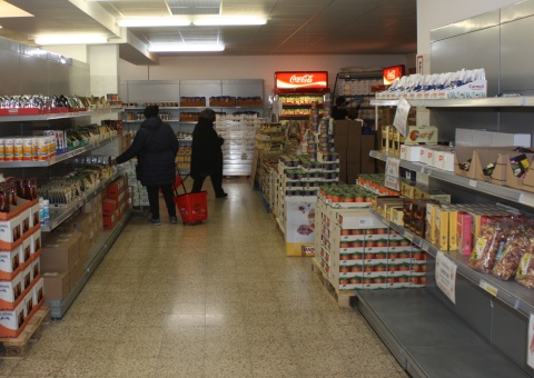 Foto zeigt das Innere eines Sozialmarkts, der im wesentlichen wie ein Supermarkt aufgebaut ist. Produkte stapeln sich auf Regalen und Paletten und zwei Personen sind umhergehend zu sehen.