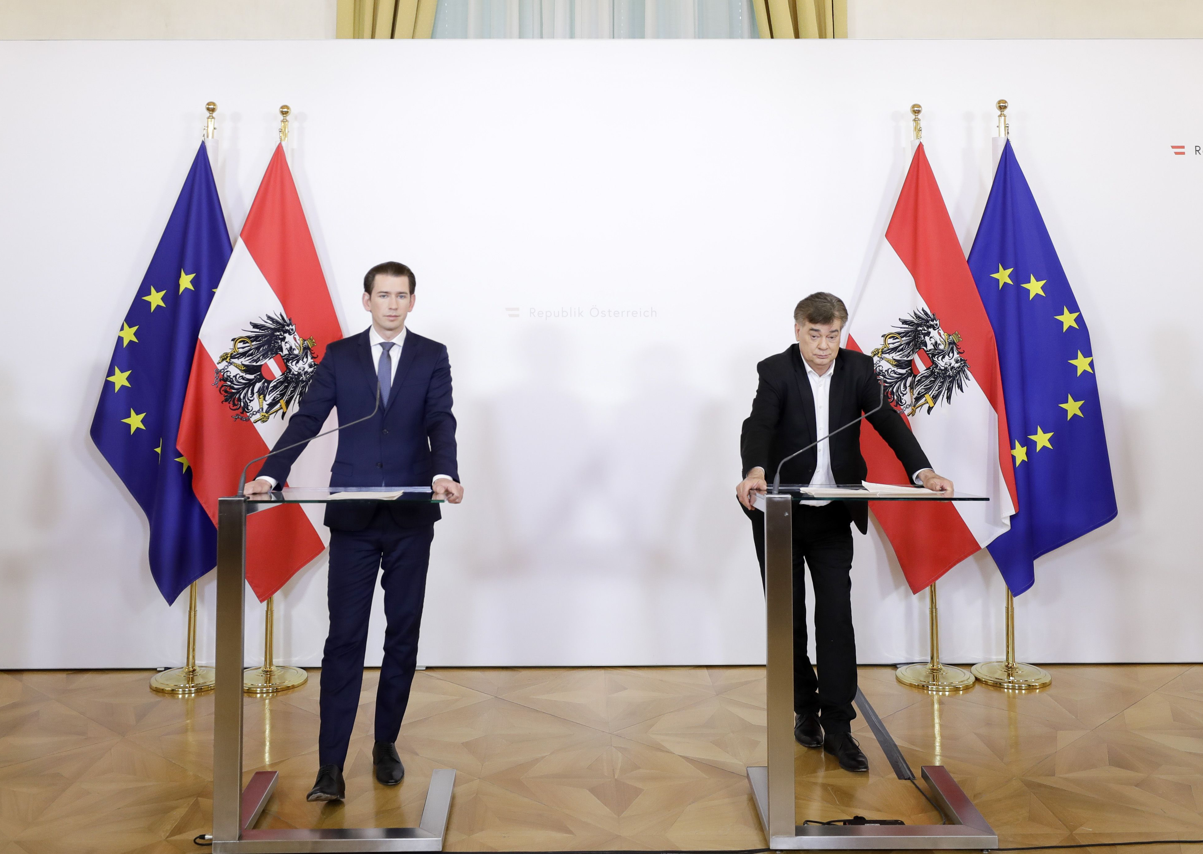 An zwei Rednerpulten zu sehen sind Sebastian Kurz (links) und Werner Kogler (rechts). Im Hintergrund sind zwei EU Fahnen und zwei Österreich Fahnen aufgestellt.