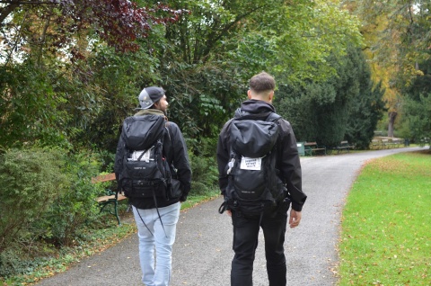 Die beiden Streetworker Viktor Knebel und Bruno Benyahia sind von hinten beim Rundgang im Grazer Stadtpark zu sehen. Sie tragen schwarze Rucksäcke mit der Aufschrift "Jugend Street Work".