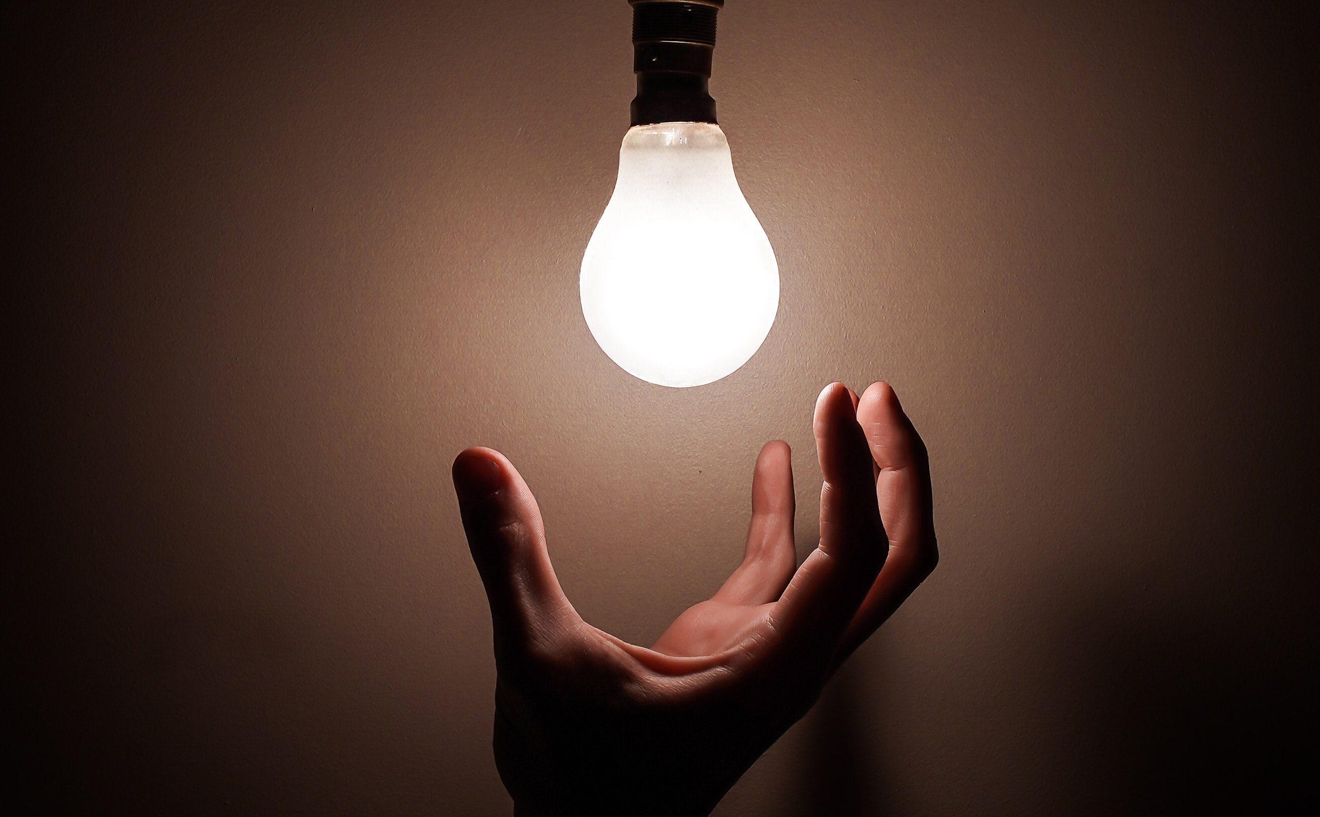 Strom- und Gasrechnungen: Zu sehen ist eine Hand, die dabei ist eine leuchtende Glühbirne anzufassen.