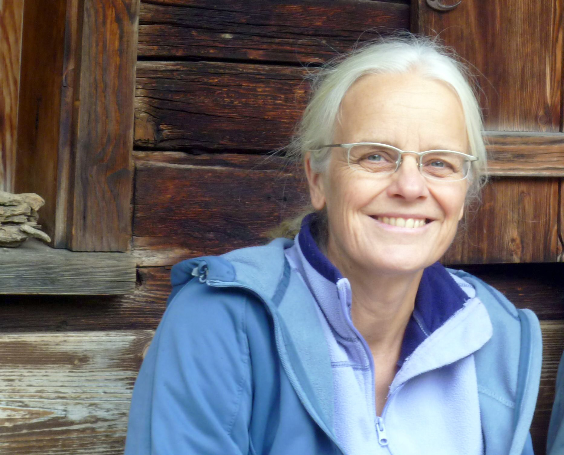 Wirtschaftsautorin Ulrike Herrmann sitzt an eine Holzwand gelehnt und blickt lächelnd in die Kamera.