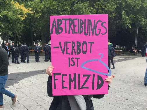 Eine Frau hält ein Schild vor ihr Gesicht, darauf steht: Abtreibungsverbot ist Femizid.