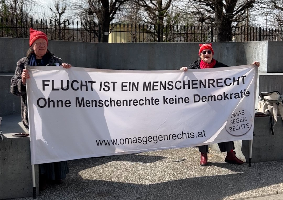 Auf dem Foto sind die Omas gegen Rechts mit einem Banner bei ihrer Mahnwache am Ballhausplatz zu sehen. Auf dem Banner steht "Flucht ist ein Menschenrecht".