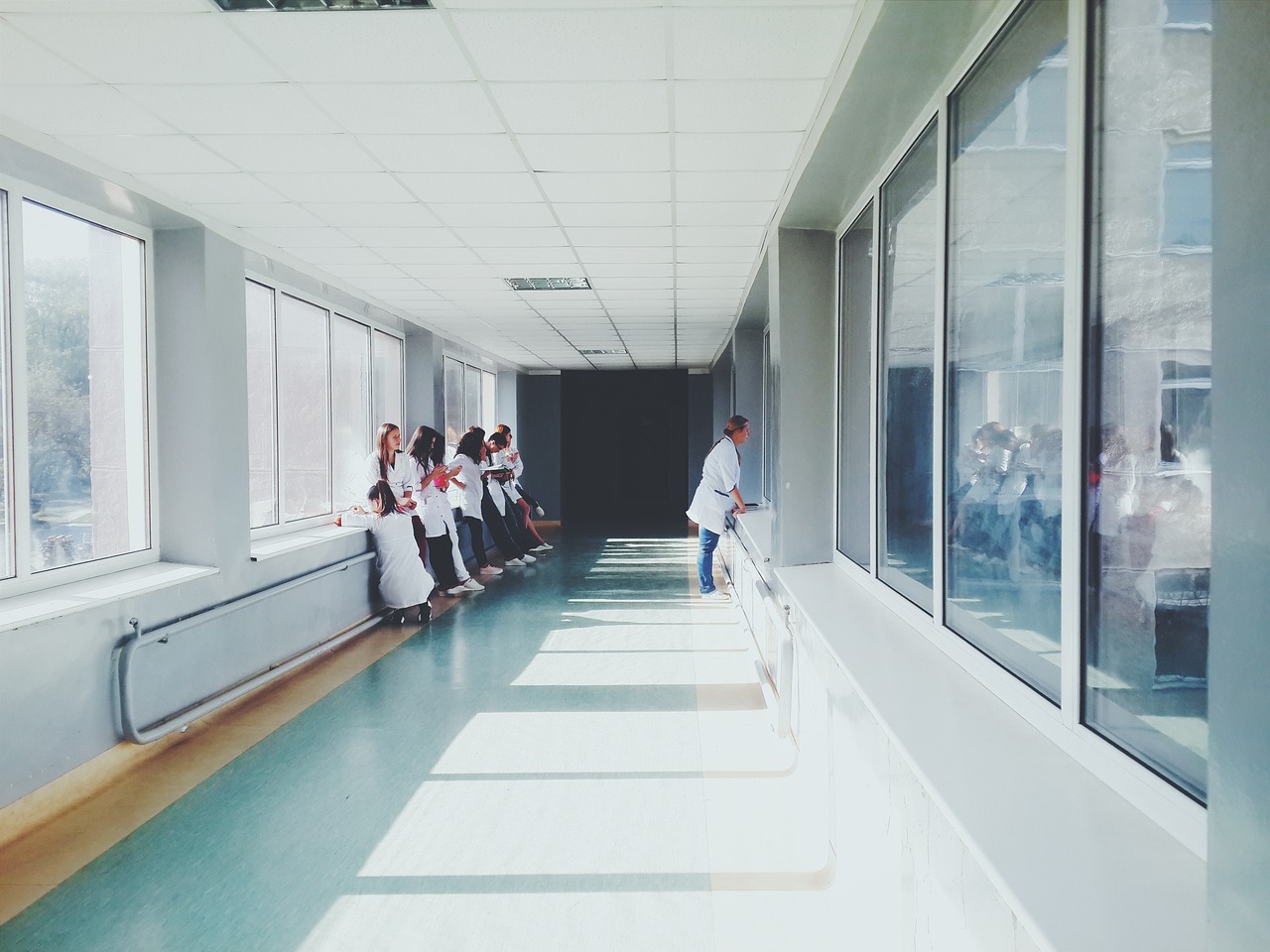 Rassismus im Gesundheitsbereich: Ein langer Gang in einem Krankenhaus, wo Gesundheitspersonal steht und Pause macht. Eine Frau sieht aus dem Fenster.