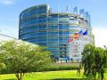 Das Europaparlament in Straßburg ist zu sehen. Vor dem gläsernen Gebäude ist Rasen und Bäume zu sehen. Ebenfalls die Flaggen der Mitgliedsstaaten. Es geht im Beitrag um einen Klima-Check der österreichischen EU-Parlamentsparteien.