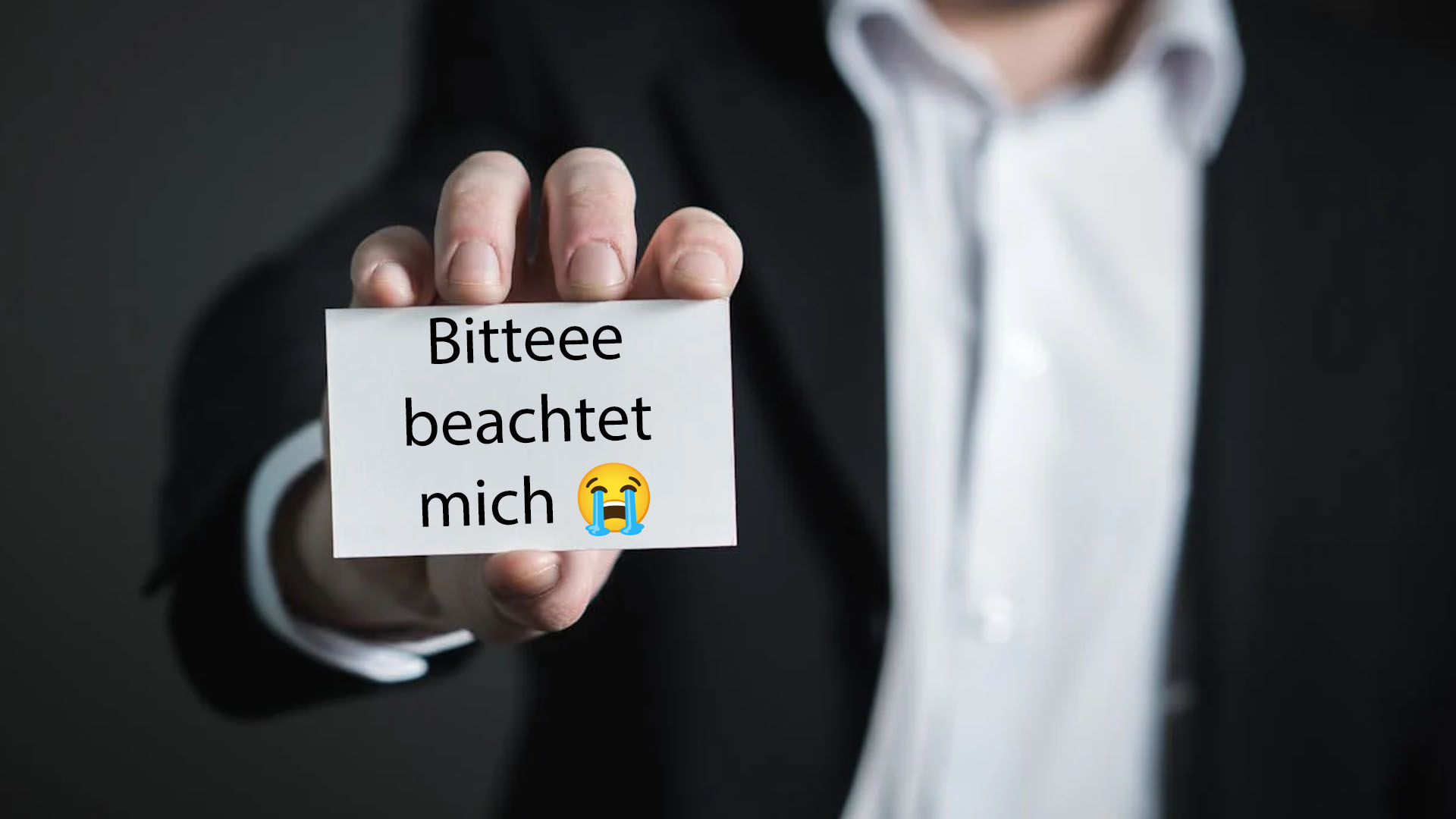 Martin Sellner will Aufmerksamkeit von Medien. (Symbolbild: Ein Mann hält eine Karte in die Kamera auf der steht: "Bitteee beachtet mich [Heul-Emoji]")