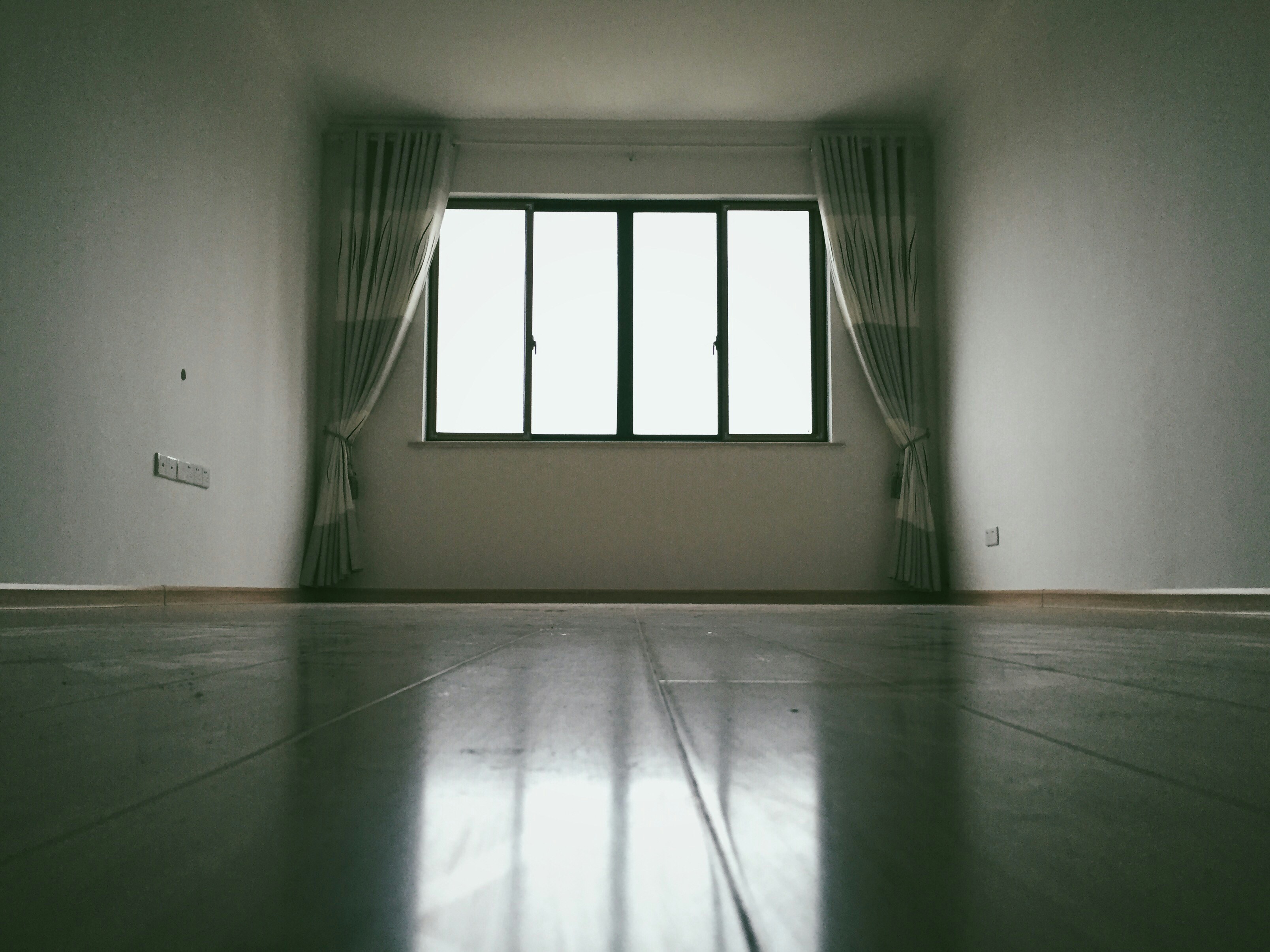 Das Bild zeigt ein leeres Zimmer, an dessen Ende Fenster zu sehen sind. Licht scheint durch die Fenster in den Wohnraum. Bebildert wird ein Artikel zur Leerstandsabgabe.