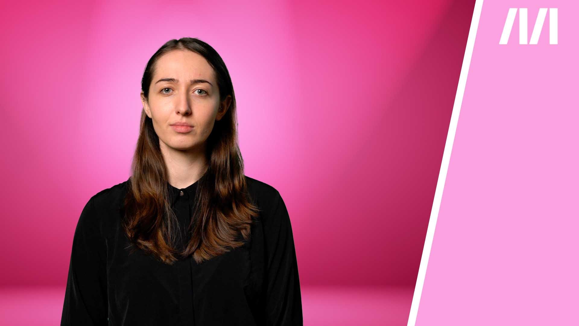 Warum erwarten Männer von Frauen, dass sie lächeln? Man sieht Kolumnistin Viktoria Eibensteiner in einer schwarzen langärmeligen Bluse, sie blickt ernst in die Kamera. Der Hintergrund ist pink.