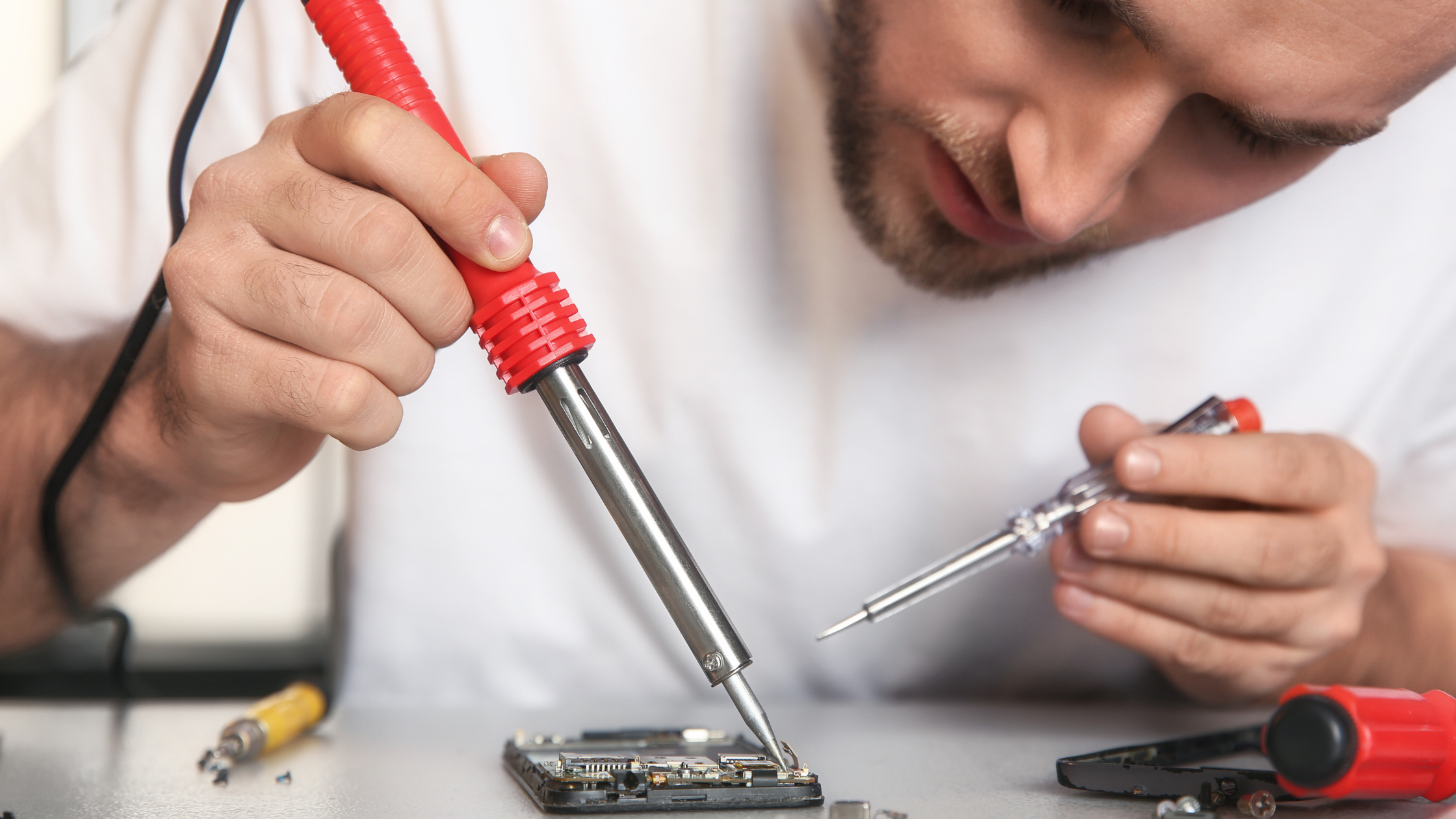 Ein Mann verwendet einen Lötkolben, um ein Handy zu reparieren.