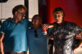 Drei Fernfahrer stehen Schulter an Schulter vor ihren Trucks im Licht der Scheinwerfer auf der Raststätte und trinken gemeinsam ein Bier